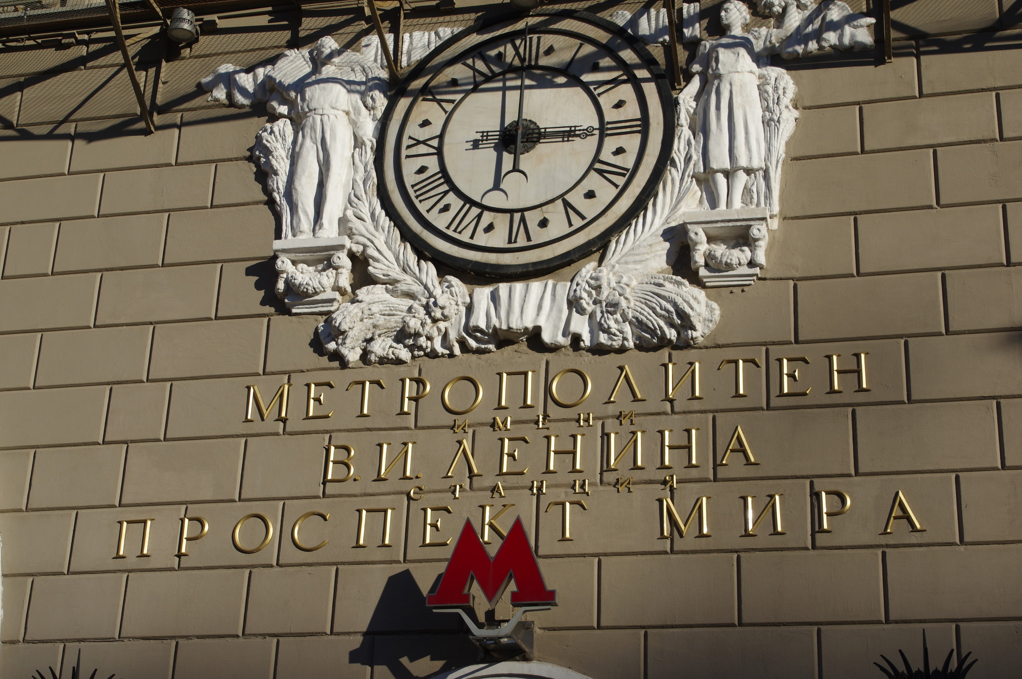 Часы, украшенные барельефом с изображением мужчины и женщины на фасаде наземного вестибюля станции «Проспект Мира» Кольцевой линии